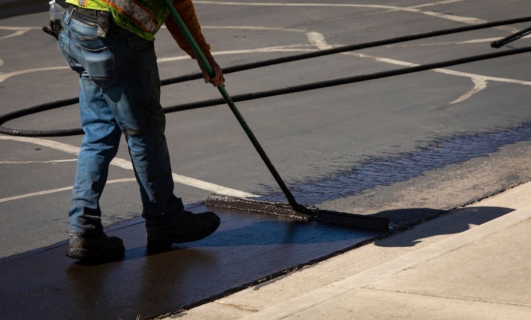 Worker brushing sealcoat along an edge in Dallas–Fort Worth, TX — Blackland Asphalt